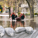 Men in waders pull a dinghy through flood water sandbags sit in the foreground
