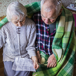 An elderly couple sit together, wrapped in a blanket, reading an energy bill.